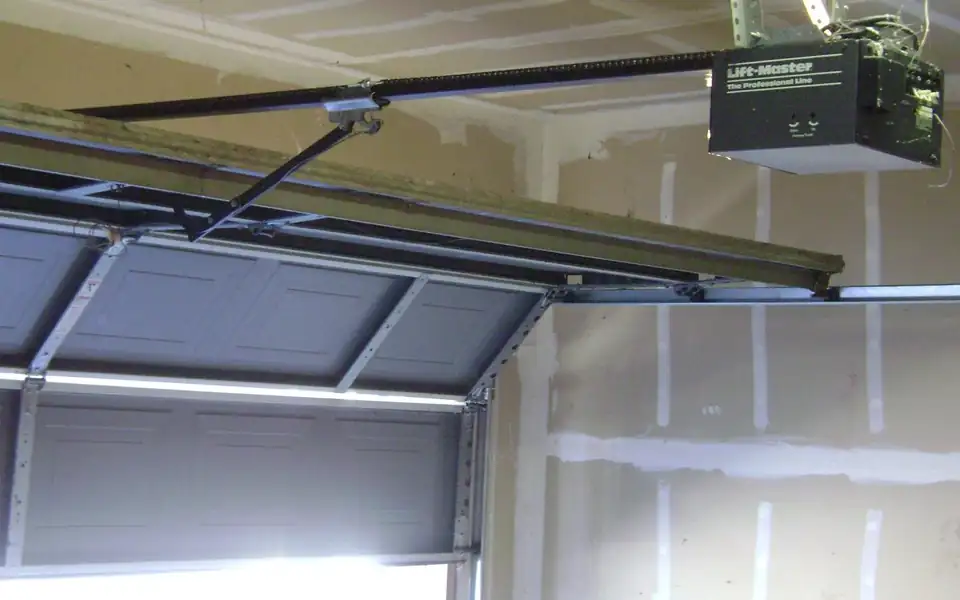 Ceiling-mounted garage door opener with its rail and a partly open door
