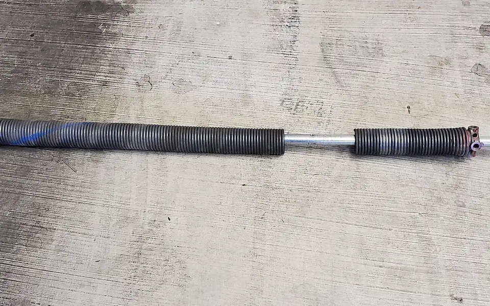 A torsion spring assembly removed from a garage door, with the broken spring visible